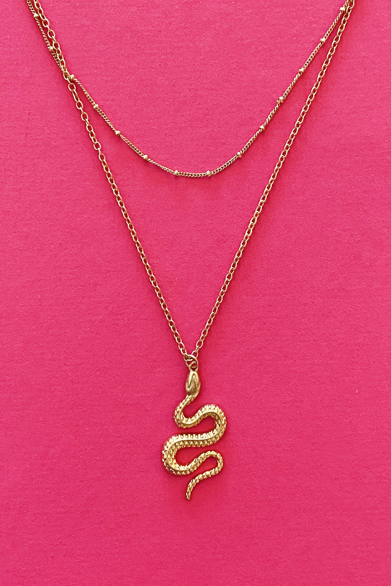 gold double layer necklace with snake pendant displayed on pink background