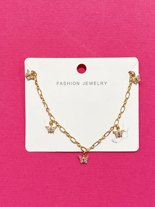 The butterfly row anklet in its packaging on a hot pink background.