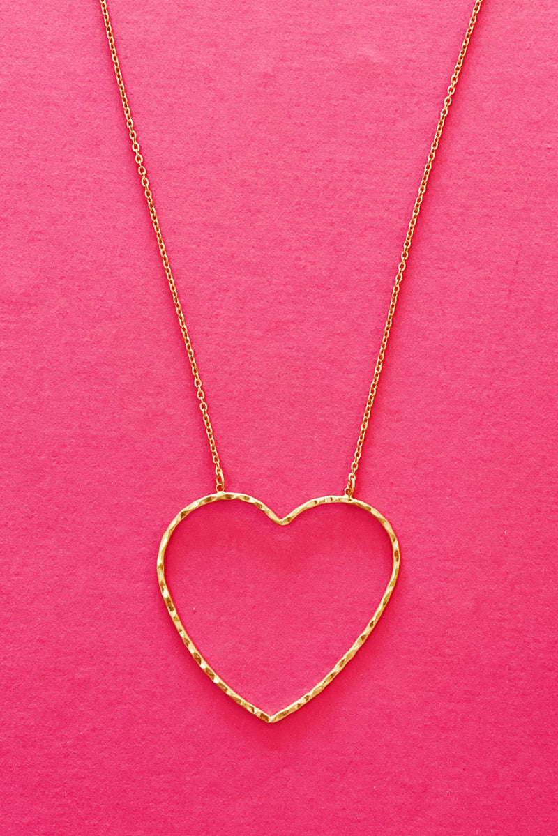 gold chain necklace with hammered heart pendant displayed on hot pink background
