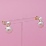 Pair of pearl earrings on a clear stand against a pink background