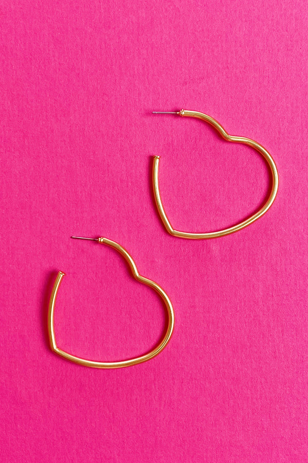 gold heart hoop earrings displayed on pink background