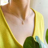 Person wearing a gold necklace with a small pendant, wearing a yellow top.