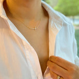 Person wearing a gold necklace with a cross pendant, blurred green background