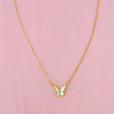 A white butterfly pendant necklace on a gold chain, displayed against a pink background.